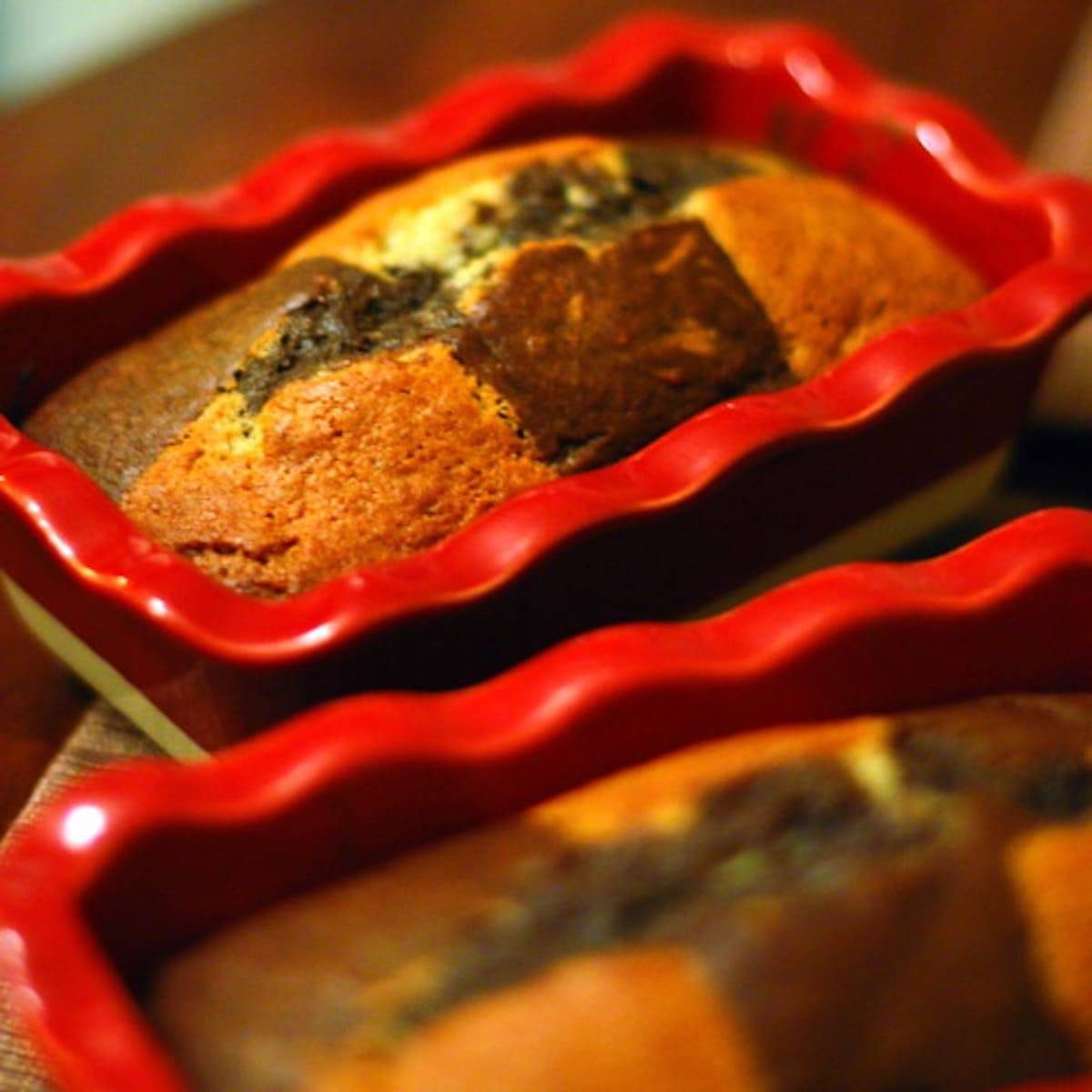Two loaves of chocolate checkered banana bread in red baking dishes.