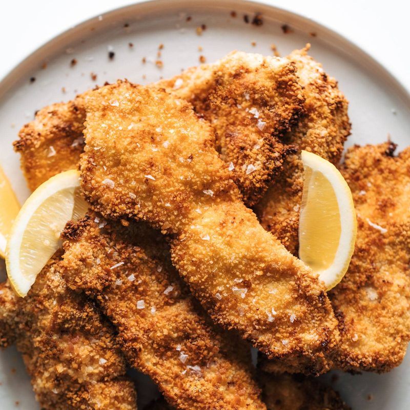 Crispy chicken cutlets on a plate with lemon wedges.