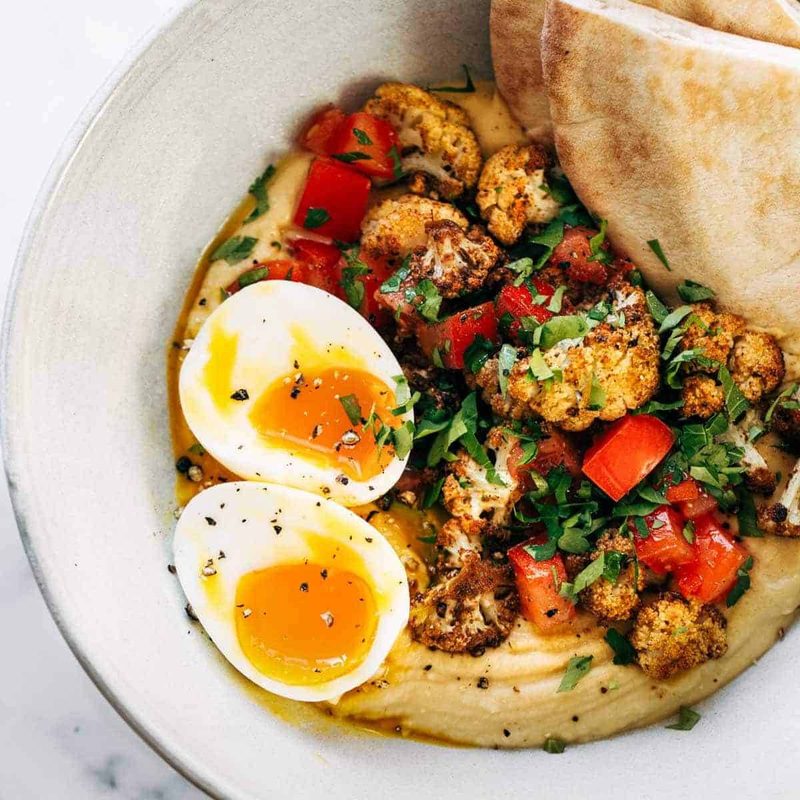 Hummus, roasted cauliflower, eggs and bread in a bowl.