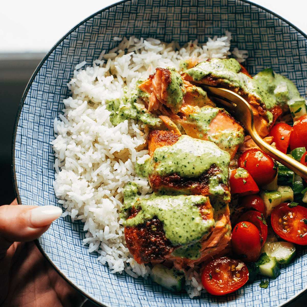 Salmon in a bowl with basil sauce, rice, and tomato salad.