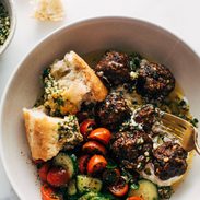 Meatballs in a bowl with a tomato salad, fork, and bread