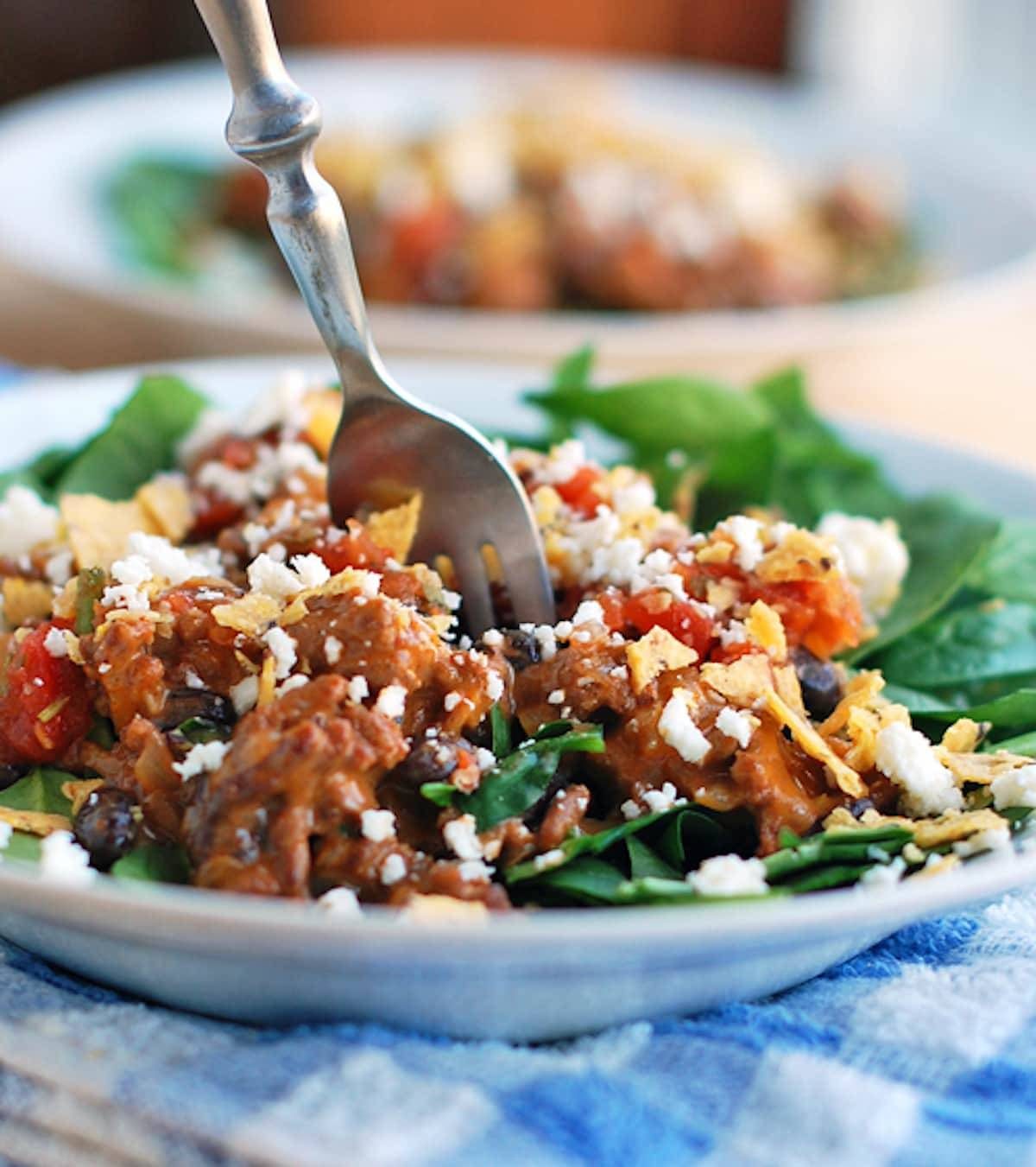 Tex-mex taco salad topped with tex-mex style ground beef on a plate with a fork.