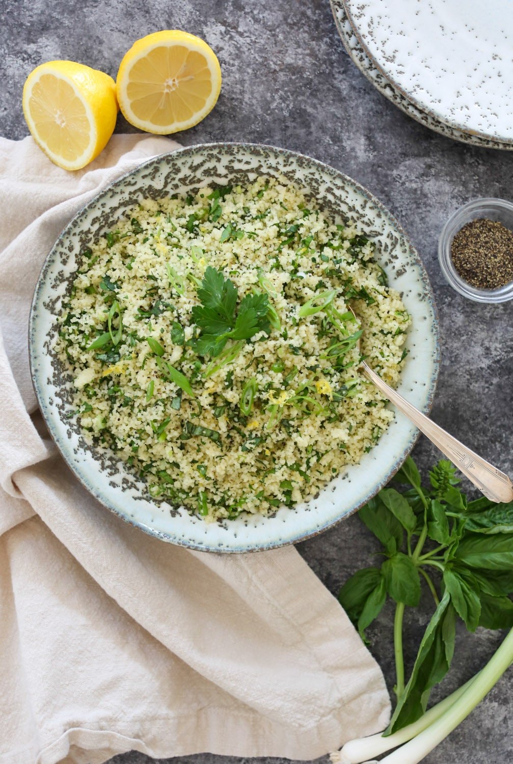 Overhead view of a bowl of Lemon-Herb Couscous with a serving spoon and decorative herbs on the side.