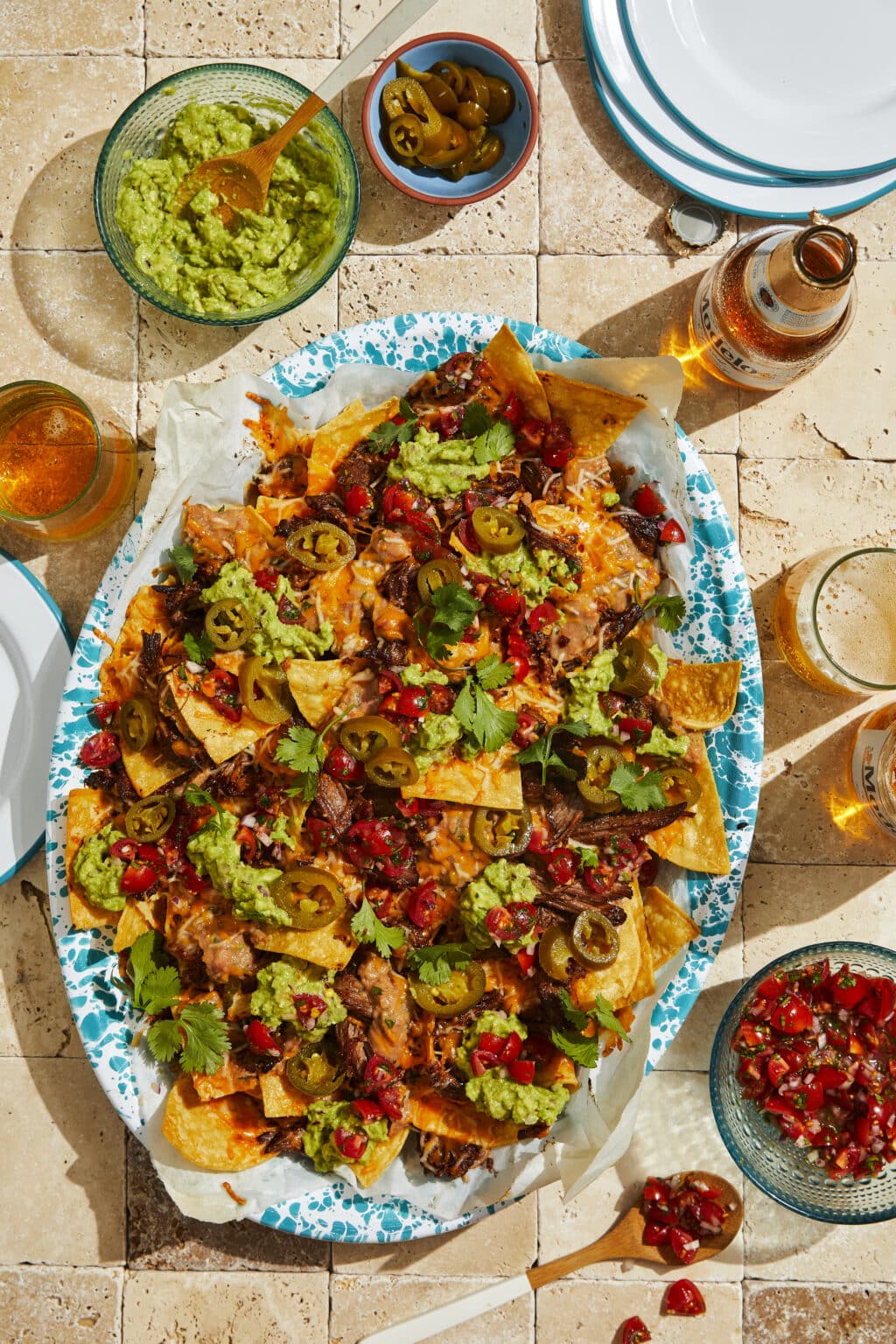 A tray of loaded short rib nachos with toppings and beer