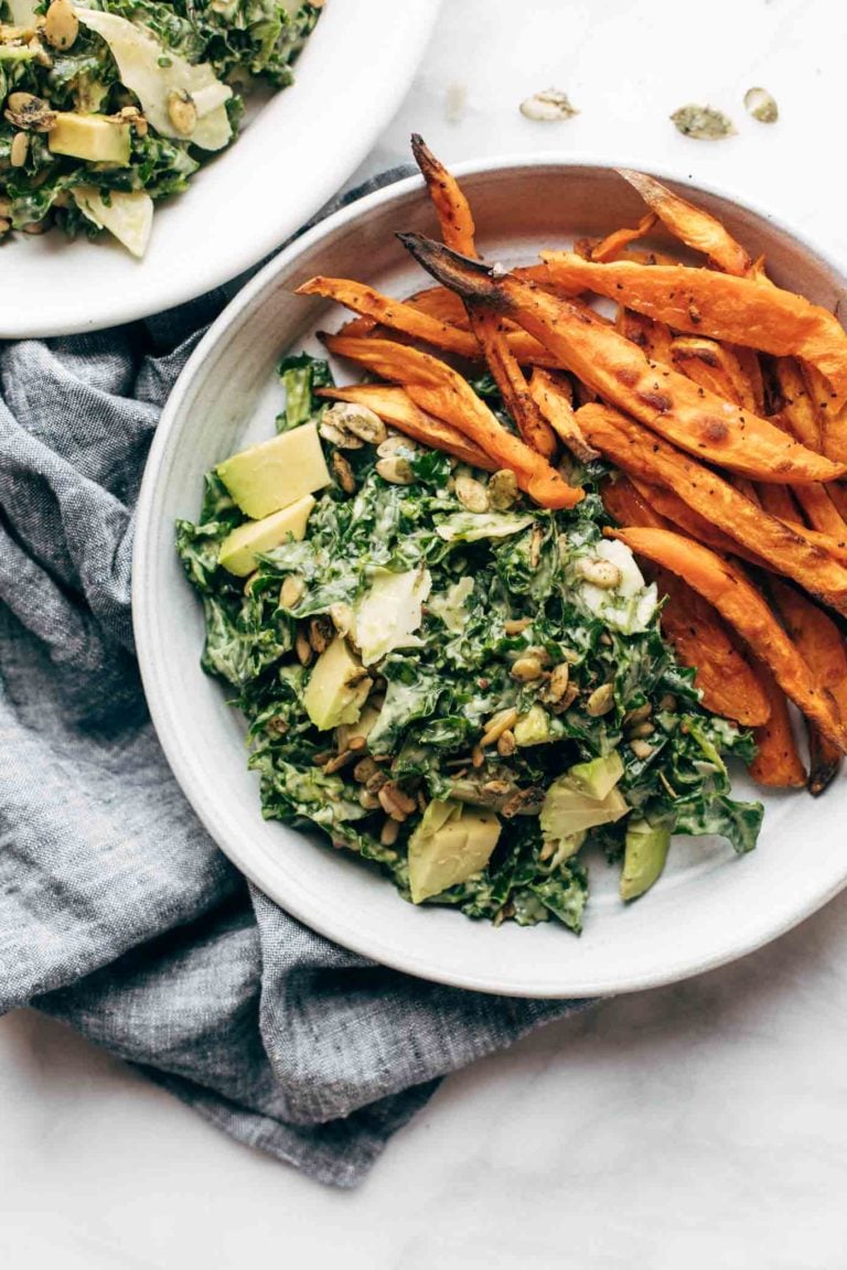 Kale caesar salad on a plate with sweet potato fries.