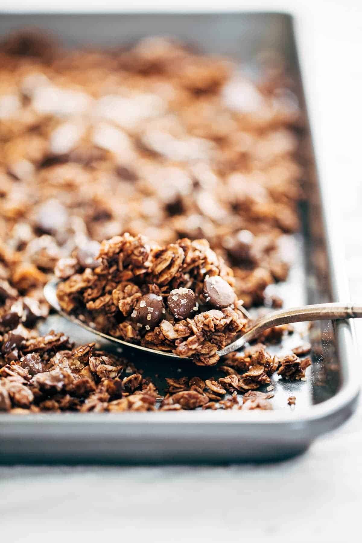 Chocolate Granola with almonds, oats, coconut flakes, chocolate chips, topped with crunchy sugar and sea salt on a pan and on a spoon.